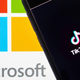 The TikTok logo on a phone in front of a screen showing the Microsoft name and logo